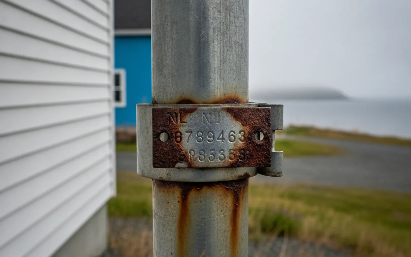 Close-up of a stamped metal HOST registration tag on an oil tank vent pipe with rust around it